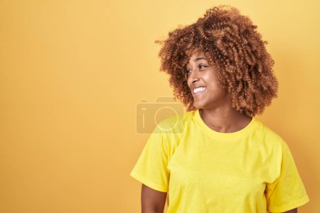 Téléchargez les photos : Jeune femme hispanique avec les cheveux bouclés debout sur fond jaune regardant de côté avec le sourire sur le visage, expression naturelle. riant confiant. - en image libre de droit