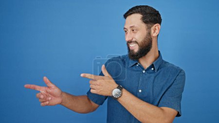 Photo for Young hispanic man smiling pointing to the side over isolated blue background - Royalty Free Image