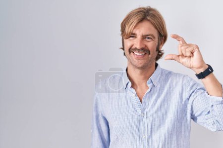 Téléchargez les photos : Homme caucasien avec moustache debout sur fond blanc geste souriant et confiant avec la main faisant signe de petite taille avec les doigts regardant et la caméra. concept de mesure. - en image libre de droit