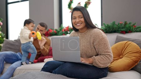 Photo for Couple and son taking care of son sitting on sofa by christmas tree working at home - Royalty Free Image