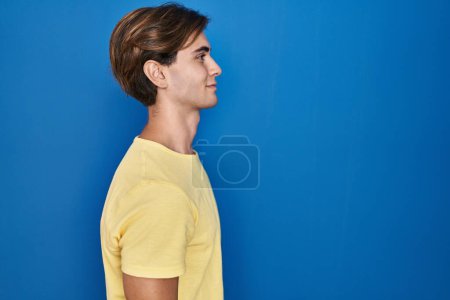 Photo for Young man standing over blue background looking to side, relax profile pose with natural face with confident smile. - Royalty Free Image