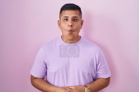 Téléchargez les photos : Jeune homme hispanique debout sur fond rose faisant visage de poisson avec des lèvres, geste fou et comique. expression drôle. - en image libre de droit