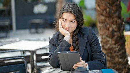 Téléchargez les photos : Jeune belle hispanique femme d'affaires en utilisant touchpad assis sur la table à la terrasse du café - en image libre de droit
