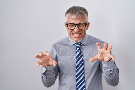 Téléchargez les photos : Homme d'affaires hispanique avec les cheveux gris portant des lunettes souriant drôle faisant griffe geste comme chat, expression agressive et sexy - en image libre de droit