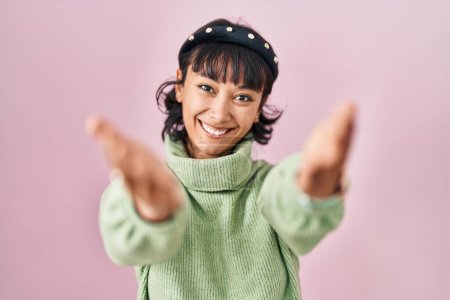 Téléchargez les photos : Young beautiful woman standing over pink background looking at the camera smiling with open arms for hug. cheerful expression embracing happiness. - en image libre de droit