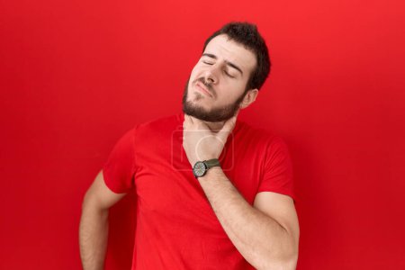 Foto de Hombre hispano joven con camiseta roja casual tocando el cuello doloroso, dolor de garganta por gripe, clod e infección - Imagen libre de derechos