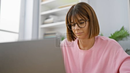 Photo for Young, beautiful, serious hispanic woman boss, a successful business professional working online at her desk in the office, concentrated on her computer laptop with glasses - Royalty Free Image