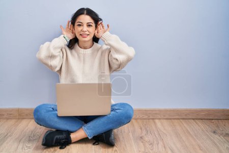 Photo for Young woman using laptop sitting on the floor at home trying to hear both hands on ear gesture, curious for gossip. hearing problem, deaf - Royalty Free Image