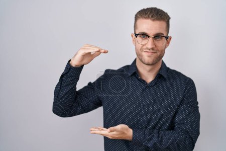 Téléchargez les photos : Jeune homme caucasien debout sur fond isolé geste avec les mains montrant grand et grand signe de taille, symbole de mesure. souriant en regardant la caméra. concept de mesure. - en image libre de droit