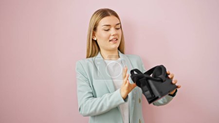 Téléchargez les photos : Jeune femme blonde ouvrière tenant des lunettes de réalité virtuelle sur fond rose isolé - en image libre de droit