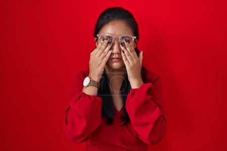 Téléchargez les photos : Asiatique jeune femme debout sur fond rouge frottant les yeux pour la fatigue et les maux de tête, somnolent et l'expression fatiguée. problème de vision - en image libre de droit