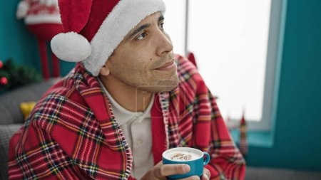 Photo for Young hispanic man drinking coffee celebrating christmas at home - Royalty Free Image