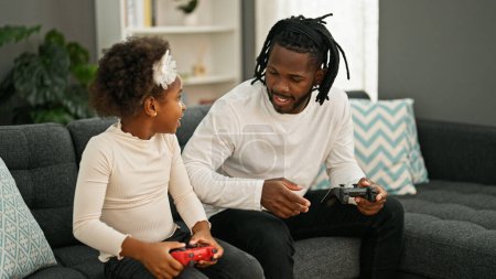 Photo for African american father and daughter playing video game sitting on sofa at home - Royalty Free Image