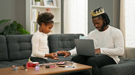 Foto de Padre e hija afroamericanos sentados en un sofá jugando mientras trabajan en casa - Imagen libre de derechos