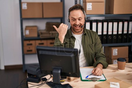 Photo for Middle age caucasian man working at small business ecommerce wearing headset pointing thumb up to the side smiling happy with open mouth - Royalty Free Image