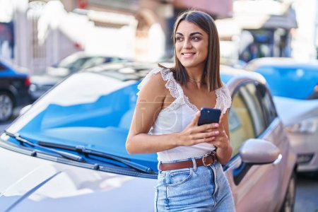 Téléchargez les photos : Jeune belle femme hispanique à l'aide d'un smartphone appuyé sur la voiture à la rue - en image libre de droit