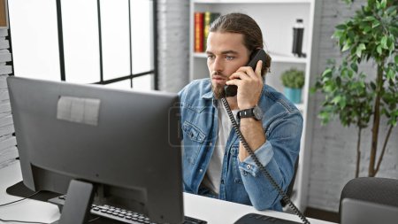 Foto de Joven trabajador de negocios hispano hablando por teléfono usando computadora en la oficina - Imagen libre de derechos
