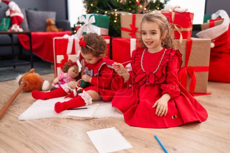 Foto de Adorables chicas dibujando en papel celebrando la Navidad en casa - Imagen libre de derechos