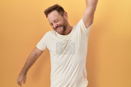 Photo for Middle age man with beard standing over yellow background dancing happy and cheerful, smiling moving casual and confident listening to music - Royalty Free Image