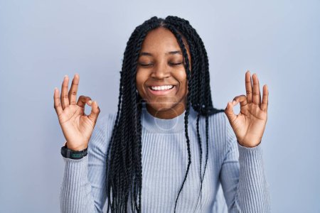 Photo for African american woman standing over blue background relaxed and smiling with eyes closed doing meditation gesture with fingers. yoga concept. - Royalty Free Image