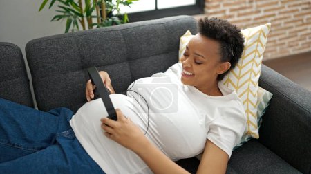 Photo for Young pregnant woman listening to music putting headphones on belly at home - Royalty Free Image
