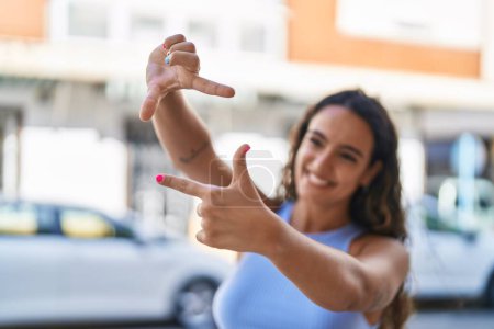 Téléchargez les photos : Jeune belle femme hispanique souriant confiant faire geste photo avec les mains à la rue - en image libre de droit