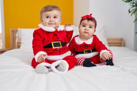 Foto de Adorable niño y niña con ropa de Navidad sentado en la cama en el dormitorio - Imagen libre de derechos