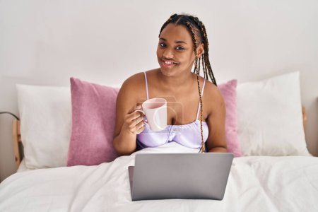 Photo for African american woman using laptop drinking coffee at bedroom - Royalty Free Image