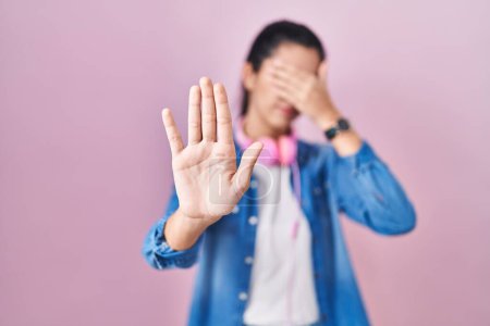 Foto de Young beautiful woman standing over pink background covering eyes with hands and doing stop gesture with sad and fear expression. embarrassed and negative concept. - Imagen libre de derechos