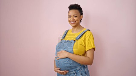 Foto de Joven embarazada sonriendo confiado tocando vientre sobre aislado rosa fondo - Imagen libre de derechos