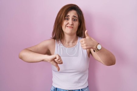 Photo for Brunette woman standing over pink background doing thumbs up and down, disagreement and agreement expression. crazy conflict - Royalty Free Image