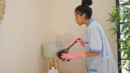 Téléchargez les photos : Femme afro-américaine nettoyer la poussière de nettoyage professionnel à la chambre d'hôtel - en image libre de droit