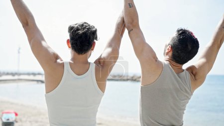 Foto de Dos parejas de hombres de pie hacia atrás con las manos levantadas en la playa - Imagen libre de derechos