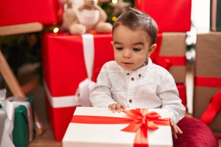 Photo for Adorable hispanic toddler unpacking christmas gift sitting on floor at home - Royalty Free Image