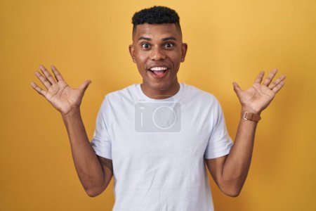 Photo for Young hispanic man standing over yellow background celebrating crazy and amazed for success with arms raised and open eyes screaming excited. winner concept - Royalty Free Image