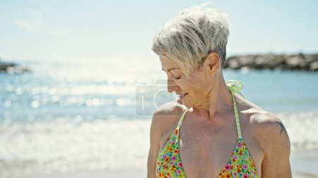 Téléchargez les photos : Moyen Age femme blonde touriste portant un bikini regardant sur le côté à la plage - en image libre de droit