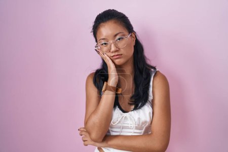 Foto de Asiática joven mujer de pie sobre rosa fondo pensamiento buscando cansado y aburrido con problemas de depresión con los brazos cruzados. - Imagen libre de derechos