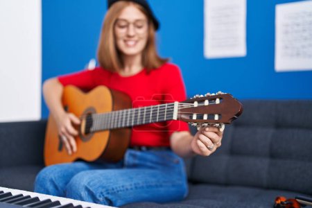 Foto de Joven pelirroja músico sonriendo confiado tocando la guitarra clásica en el estudio de música - Imagen libre de derechos