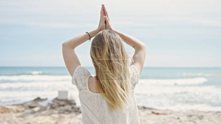 Téléchargez les photos : Jeune femme blonde touriste debout à l'envers faisant de l'exercice de yoga à la plage - en image libre de droit