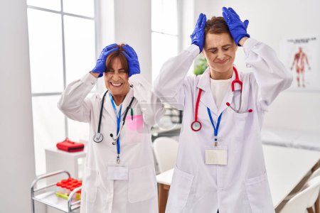 Foto de Dos mujeres con uniforme médico y estetoscopio que sufren de dolor de cabeza desesperado y estresado debido al dolor y la migraña. manos en la cabeza. - Imagen libre de derechos