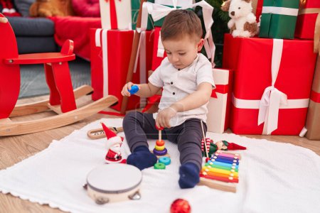 Téléchargez les photos : Adorable bambin hispanique jouant avec des jouets assis sur le sol par des cadeaux de Noël à la maison - en image libre de droit