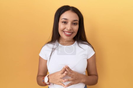 Téléchargez les photos : Jeune femme arabe portant casual t-shirt blanc sur fond jaune mains ensemble et les doigts croisés souriant détendu et joyeux. succès et optimisme - en image libre de droit