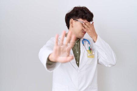 Photo for Young non binary man wearing doctor uniform and stethoscope covering eyes with hands and doing stop gesture with sad and fear expression. embarrassed and negative concept. - Royalty Free Image