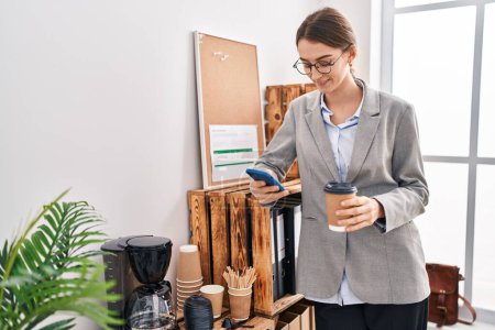 Téléchargez les photos : Young caucasian woman business worker using smartphone drinking coffee at office - en image libre de droit