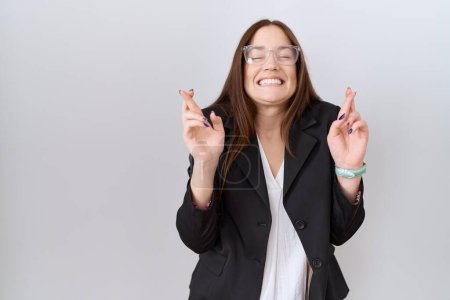 Photo for Beautiful brunette woman wearing business jacket and glasses gesturing finger crossed smiling with hope and eyes closed. luck and superstitious concept. - Royalty Free Image