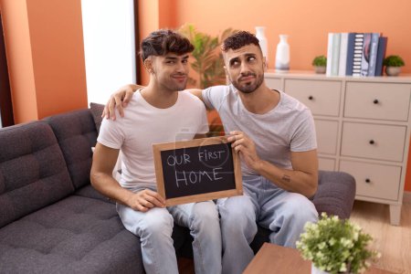 Photo for Homosexual gay couple holding blackboard with first home text smiling looking to the side and staring away thinking. - Royalty Free Image