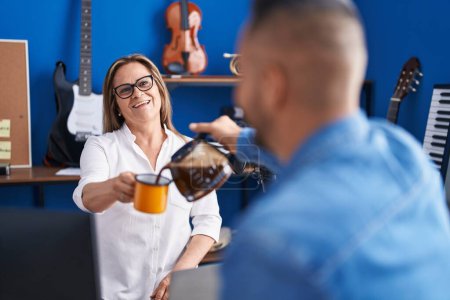 Téléchargez les photos : Man and woman musicians smiling confident drinking coffee at music studio - en image libre de droit