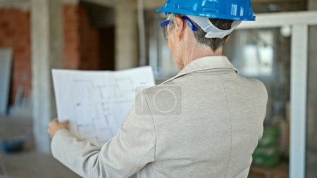 Foto de Mujer rubia de mediana edad arquitecta leyendo proyecto de casa en obra - Imagen libre de derechos