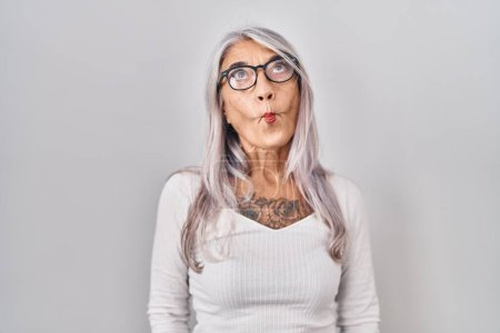 Photo for Middle age woman with grey hair standing over white background making fish face with lips, crazy and comical gesture. funny expression. - Royalty Free Image