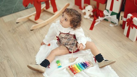 Téléchargez les photos : Adorable hispanic girl playing xylophone sitting on floor by christmas tree at home - en image libre de droit
